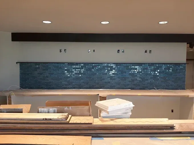 Blue glass tile backsplash under construction, wood counter, recessed lights.