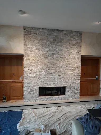 Stone fireplace with built-in shelving and cabinets on each side; construction zone, white sheet on floor.