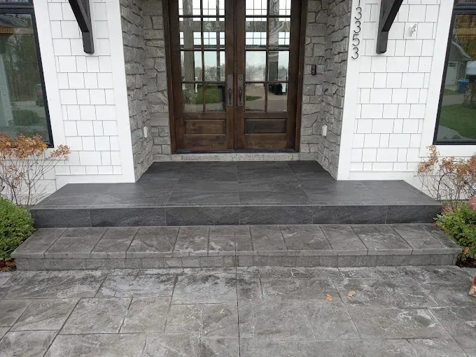 Front entrance with dark gray concrete steps leading to wooden double doors. White shingle siding.