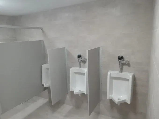 Three urinals in a public restroom with white walls and dividers.