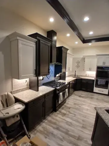Modern kitchen with gray and dark brown cabinets, stainless steel appliances, and light-colored wood-look flooring.
