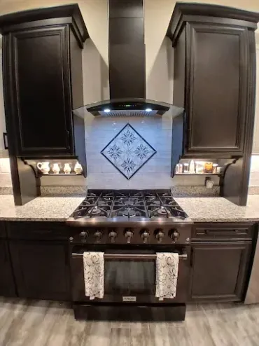Modern kitchen with dark cabinets, stovetop, and decorative backsplash.