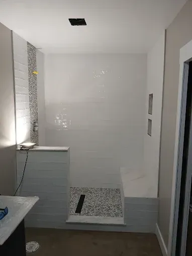 White-tiled shower with mosaic accent. Light gray bench and floor tile. Black drain.
