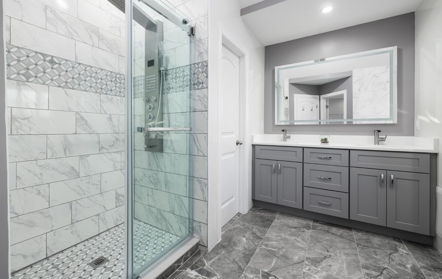 Modern bathroom with gray cabinets, marble-look tile, glass shower, and a large mirror.