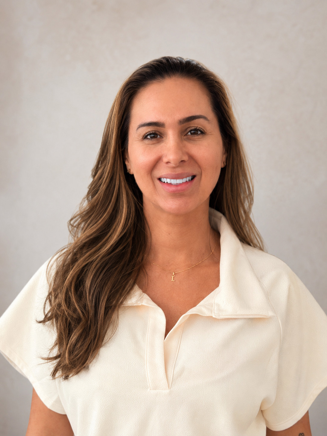 Mujer sonriente con blusa color crema sobre fondo claro.