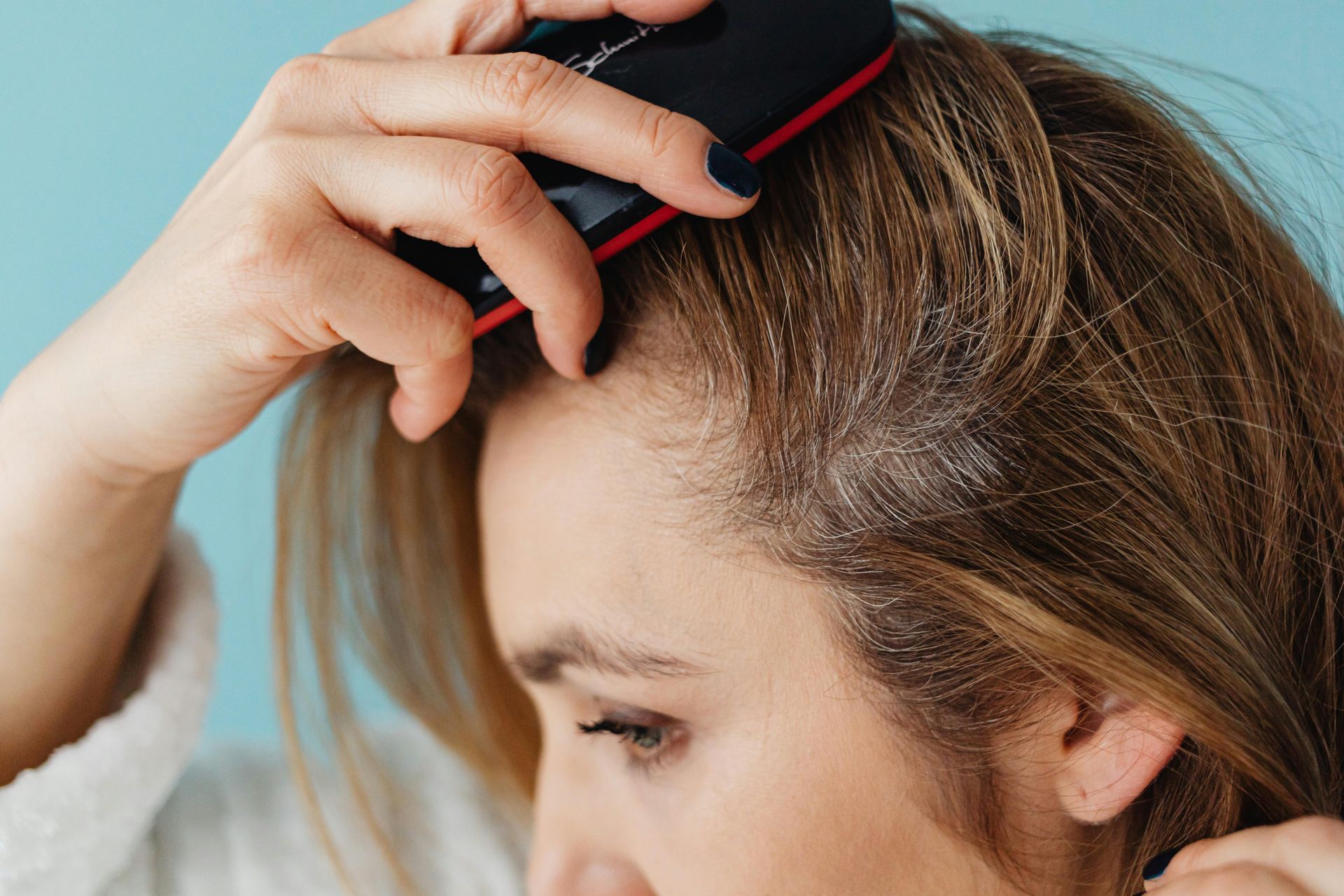 Persona peinándose la parte superior de su cabello castaño con un peine negro, vista lateral en primer plano.