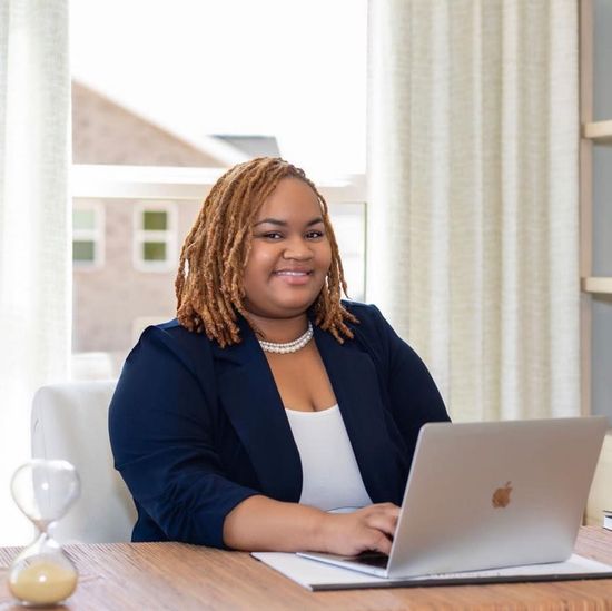 A woman is sitting at a desk with a laptop and a vase of flowers.