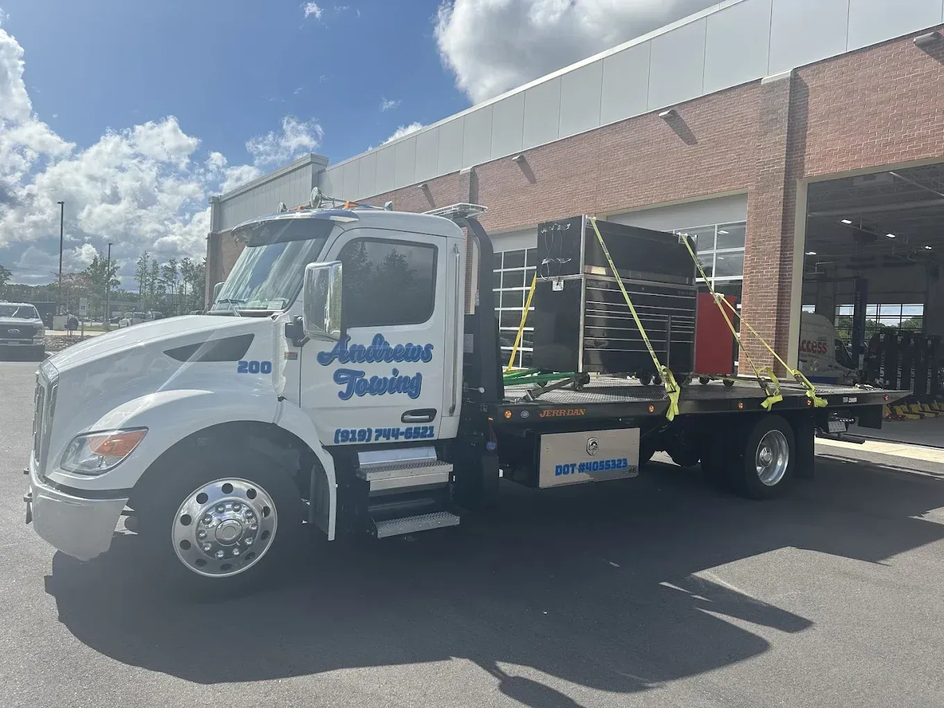 A white tow truck is parked in front of a brick building.