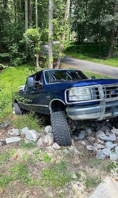 A blue truck is parked on the side of the road next to a tree.