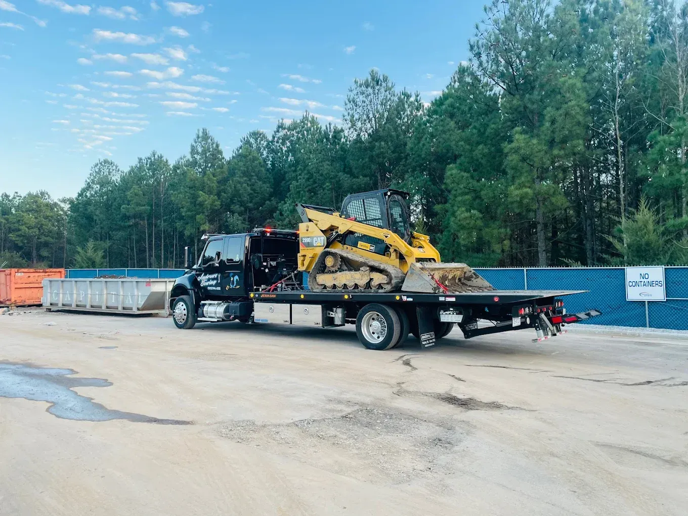 A tow truck with a bulldozer on the back is parked in a parking lot.