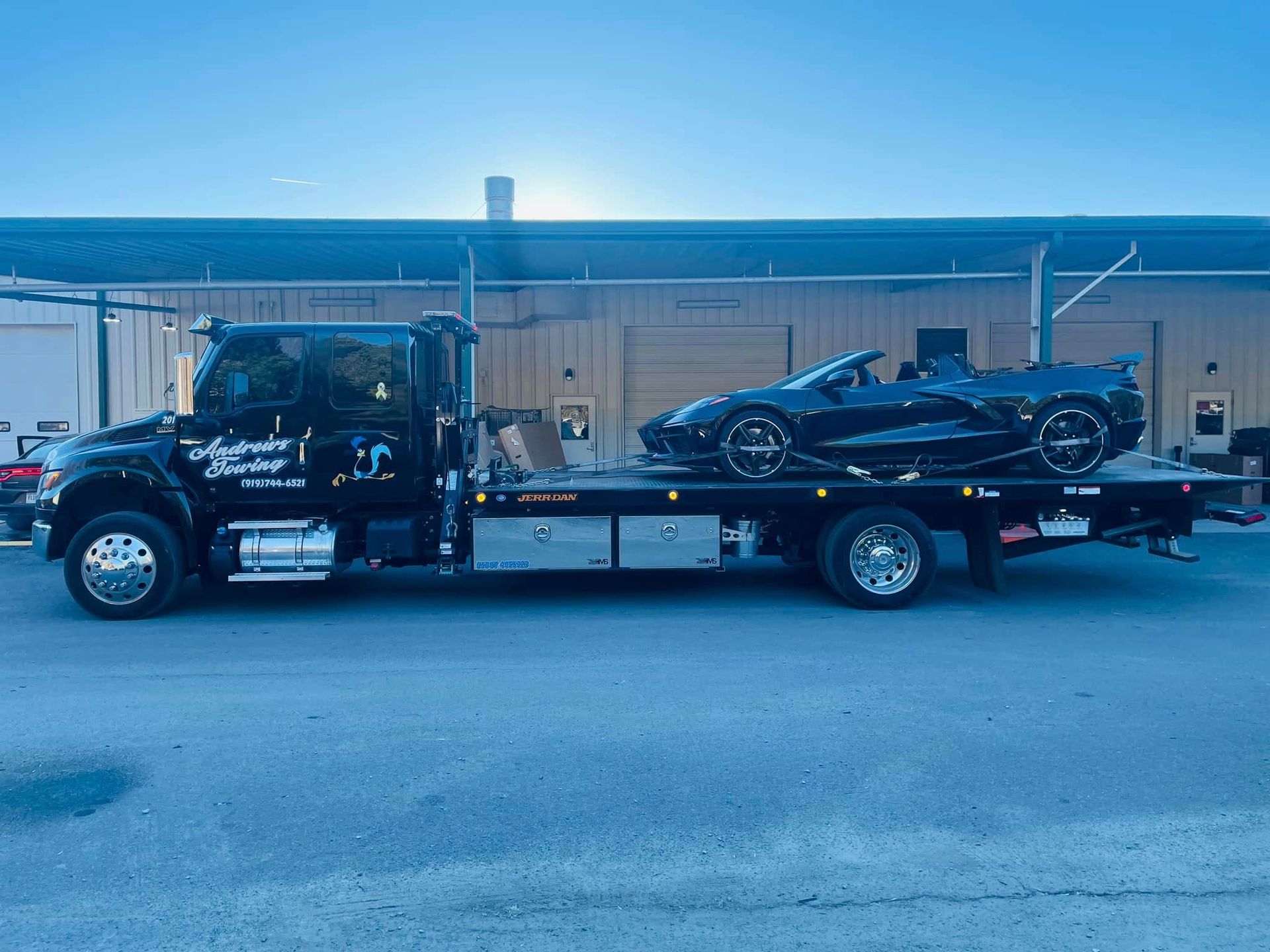 A black tow truck is towing a black sports car.