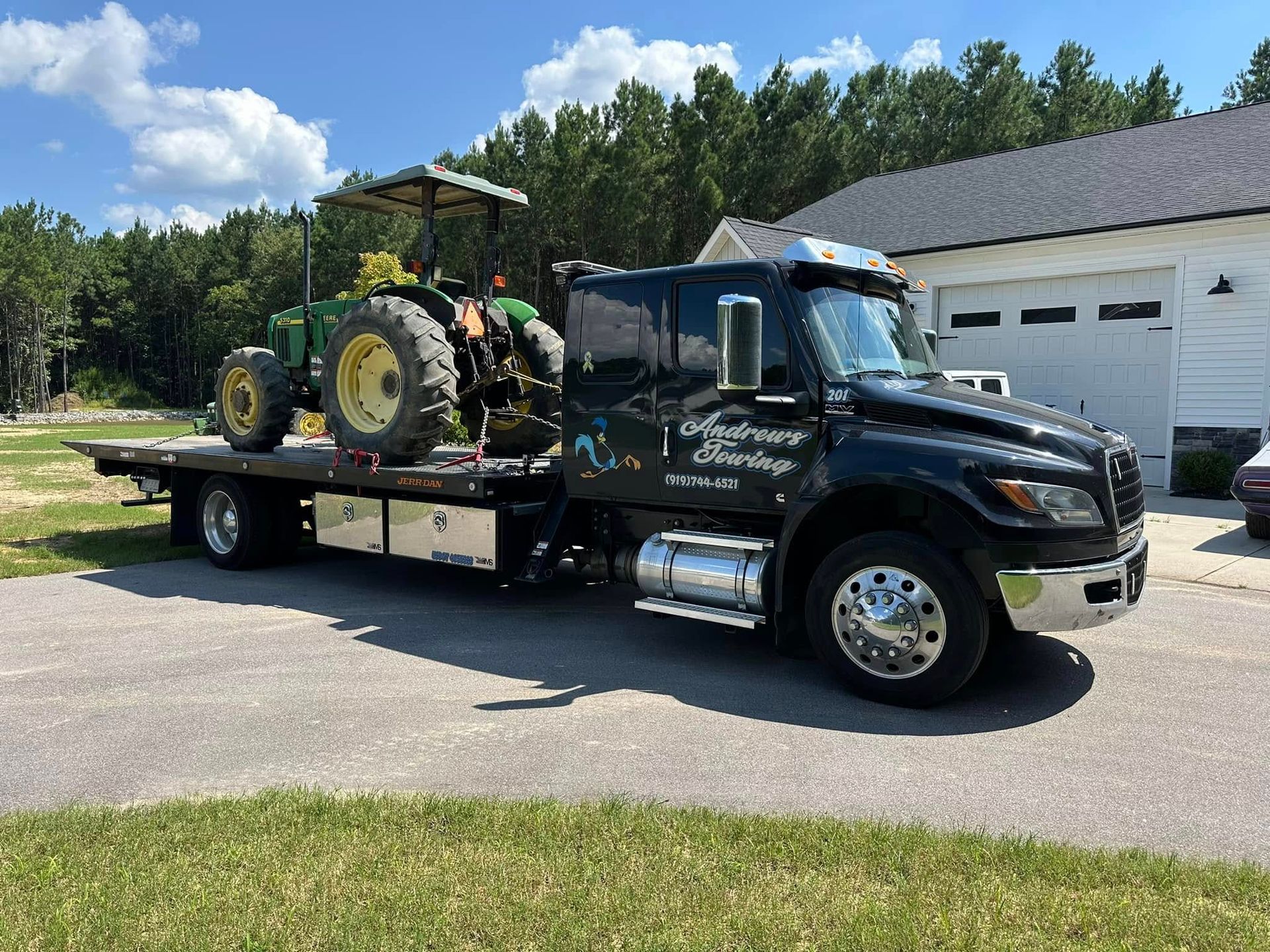 A tow truck is carrying a tractor on the back of it.