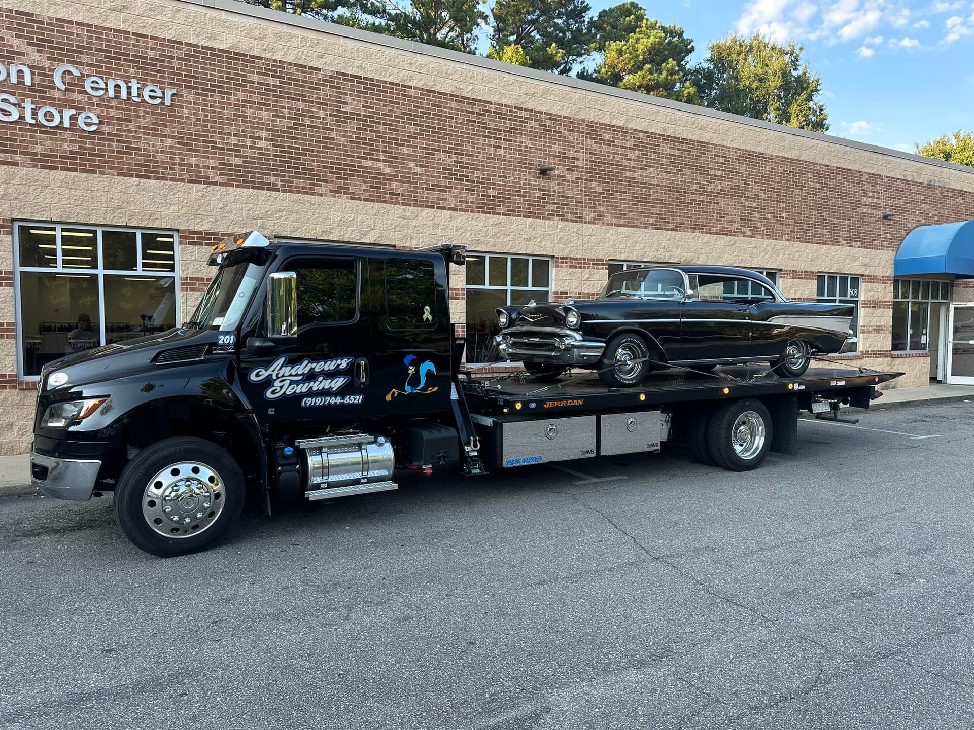 A tow truck with a car on the back is parked in front of a brick building.