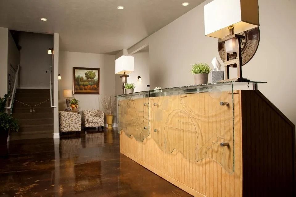 Hotel lobby with wooden front desk, staircase, chairs, and warm lighting