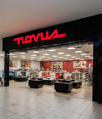 Entrance to a Movus store with a red logo on a black facade. Store displays visible inside.