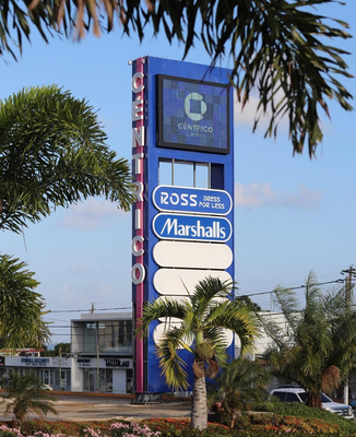 Outdoor shopping plaza sign with Ross and Marshalls logos, framed by palm trees against a blue sky.