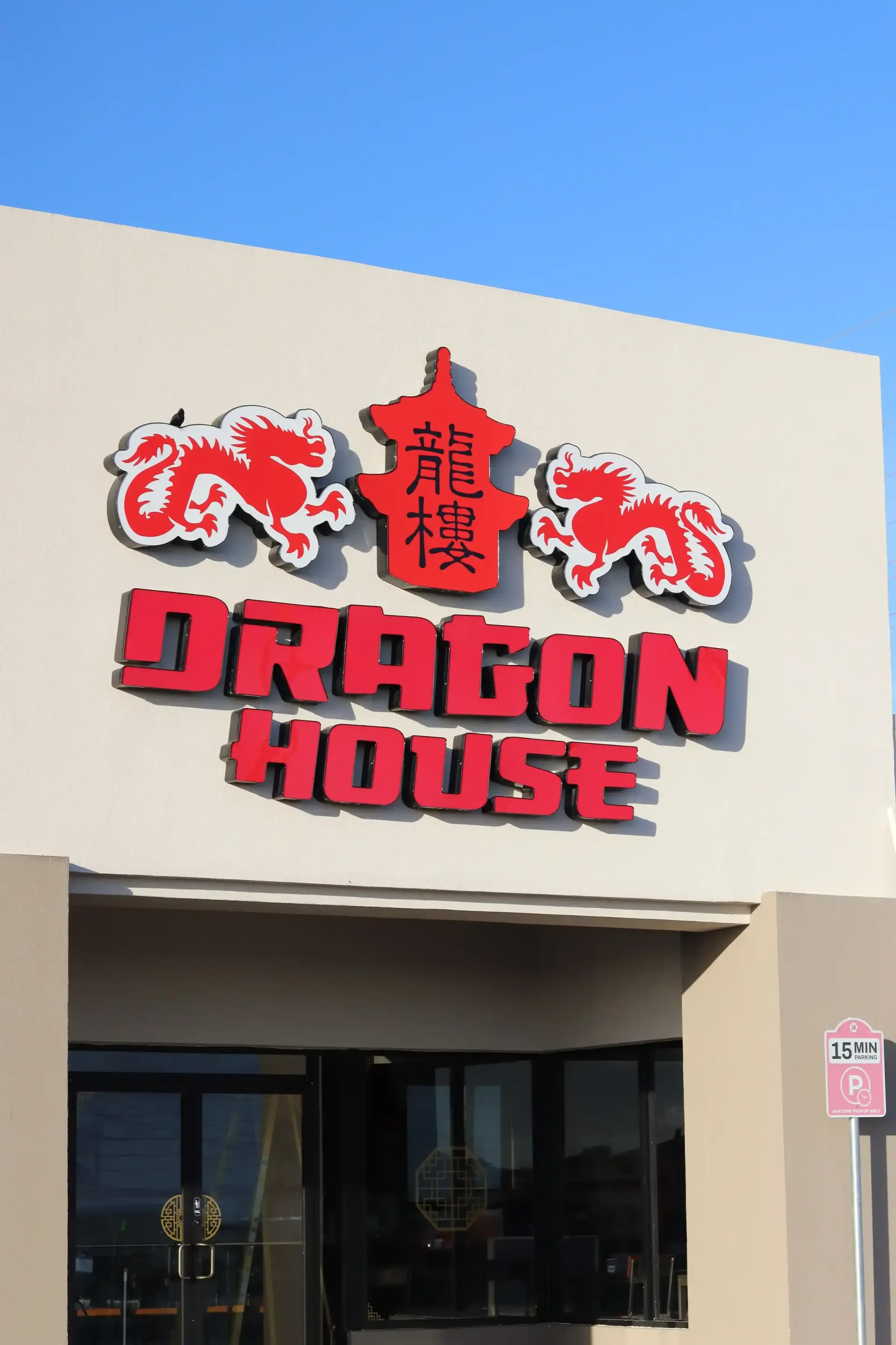 Sign for Dragon House restaurant, red text on a beige background. Features two red dragon figures and Chinese characters.
