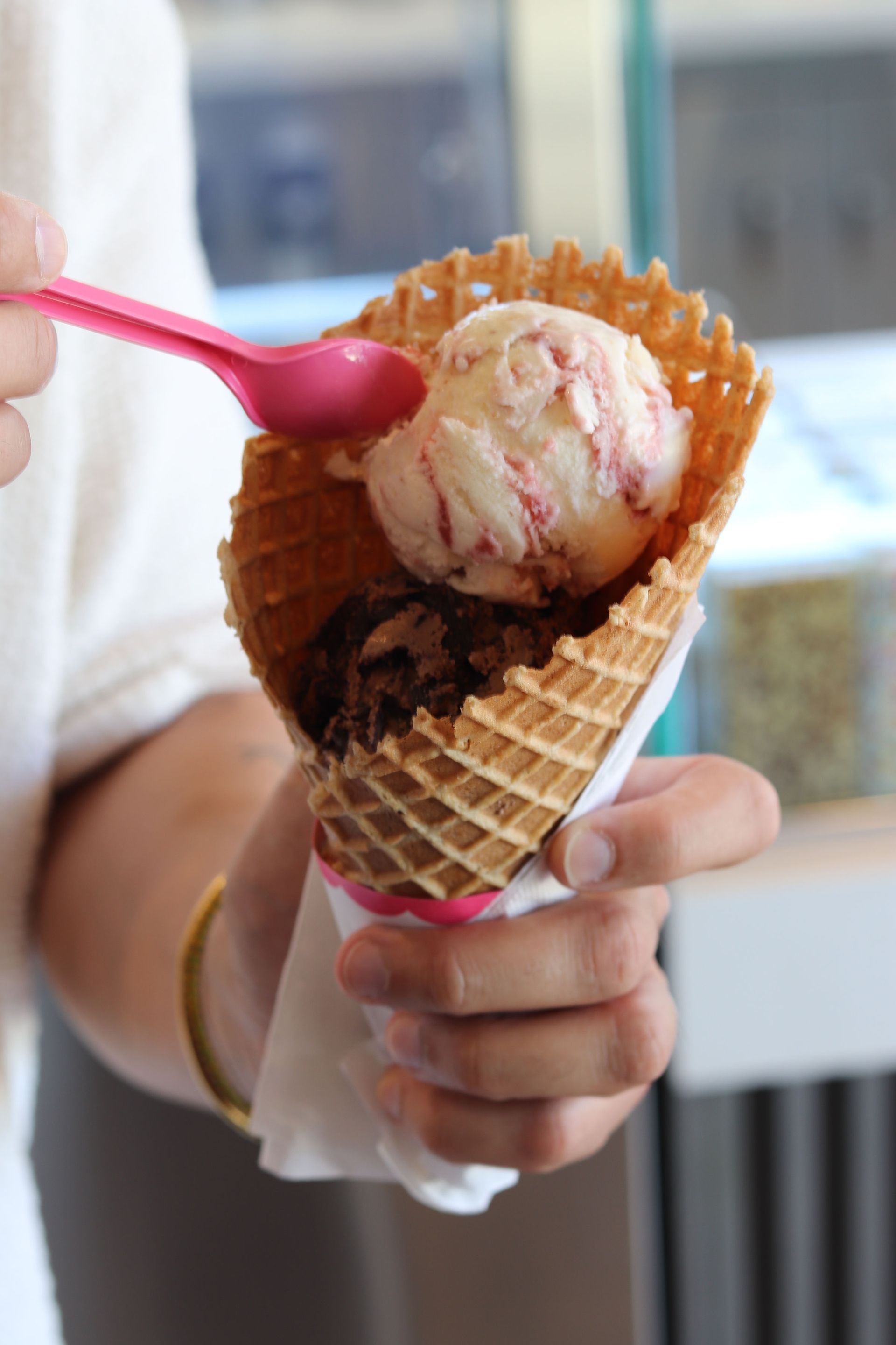 Two people smiling while holding ice cream cones in front of a pink and white abstract mural.