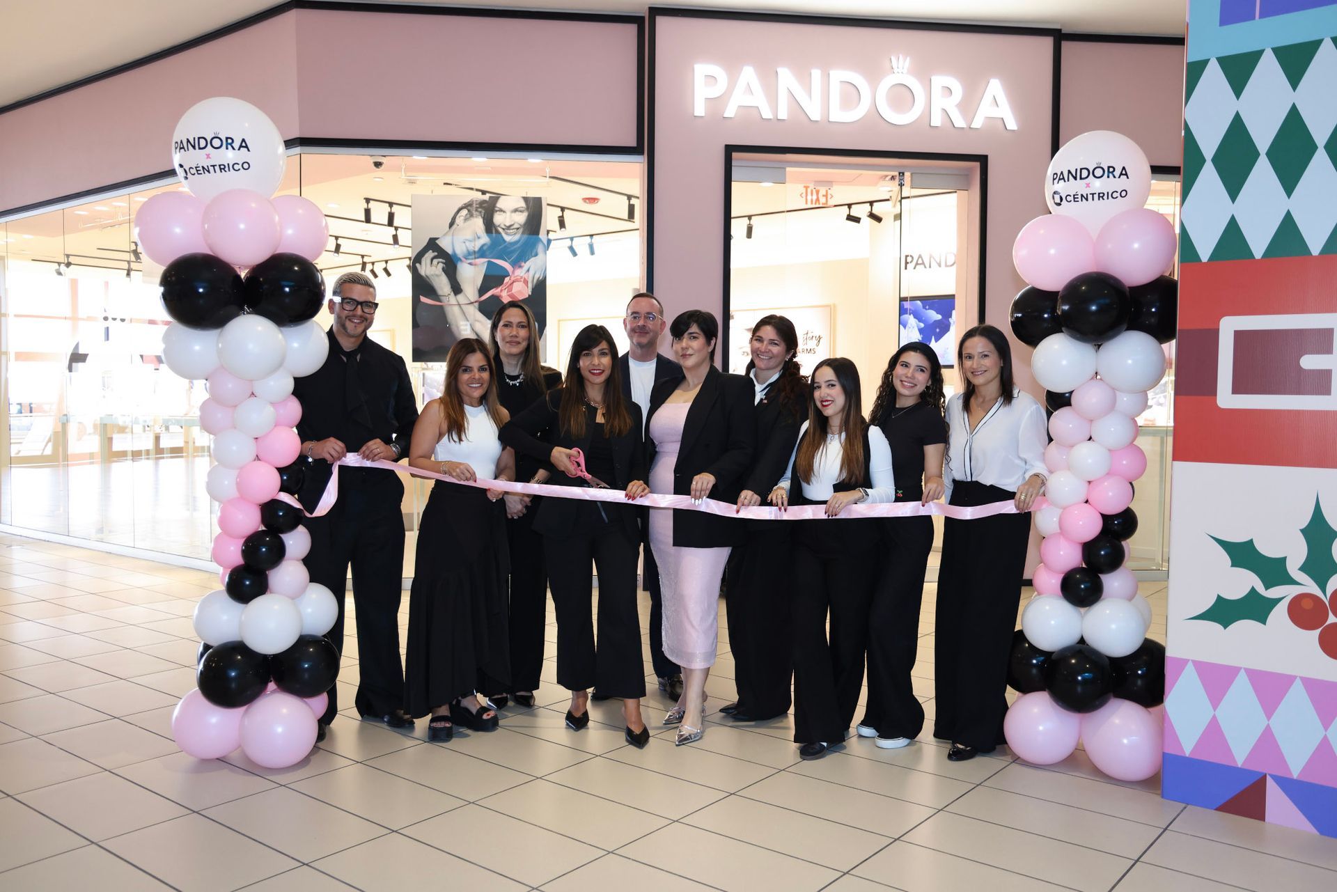 People cutting a ribbon in front of a Pandora store with balloon decorations.