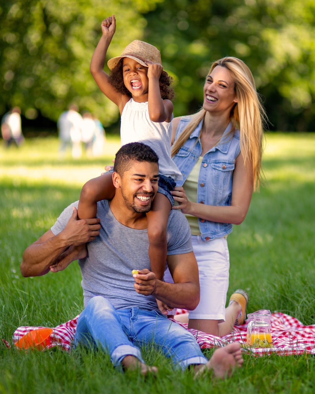 Two people sitting outdoors in swimwear and patterned clothing cover their faces with open magazines.