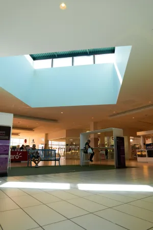 Mall interior with skylight, two people seated on benches, and storefronts.