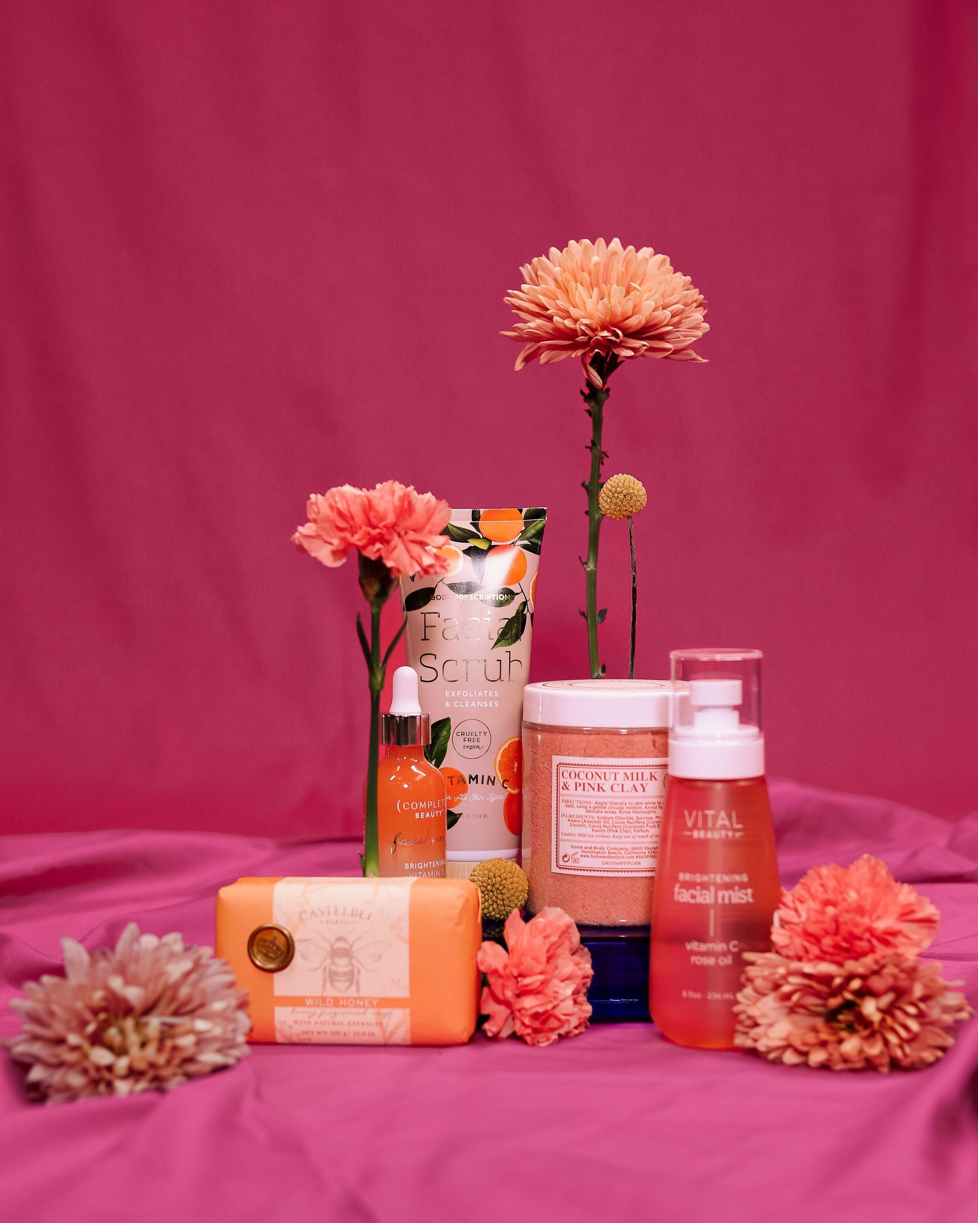 Pink skincare products and flowers arranged on a magenta backdrop.