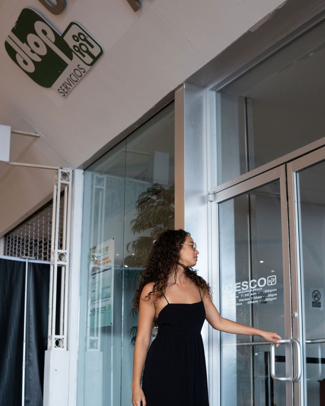 Woman in black dress opening a glass door; sign for