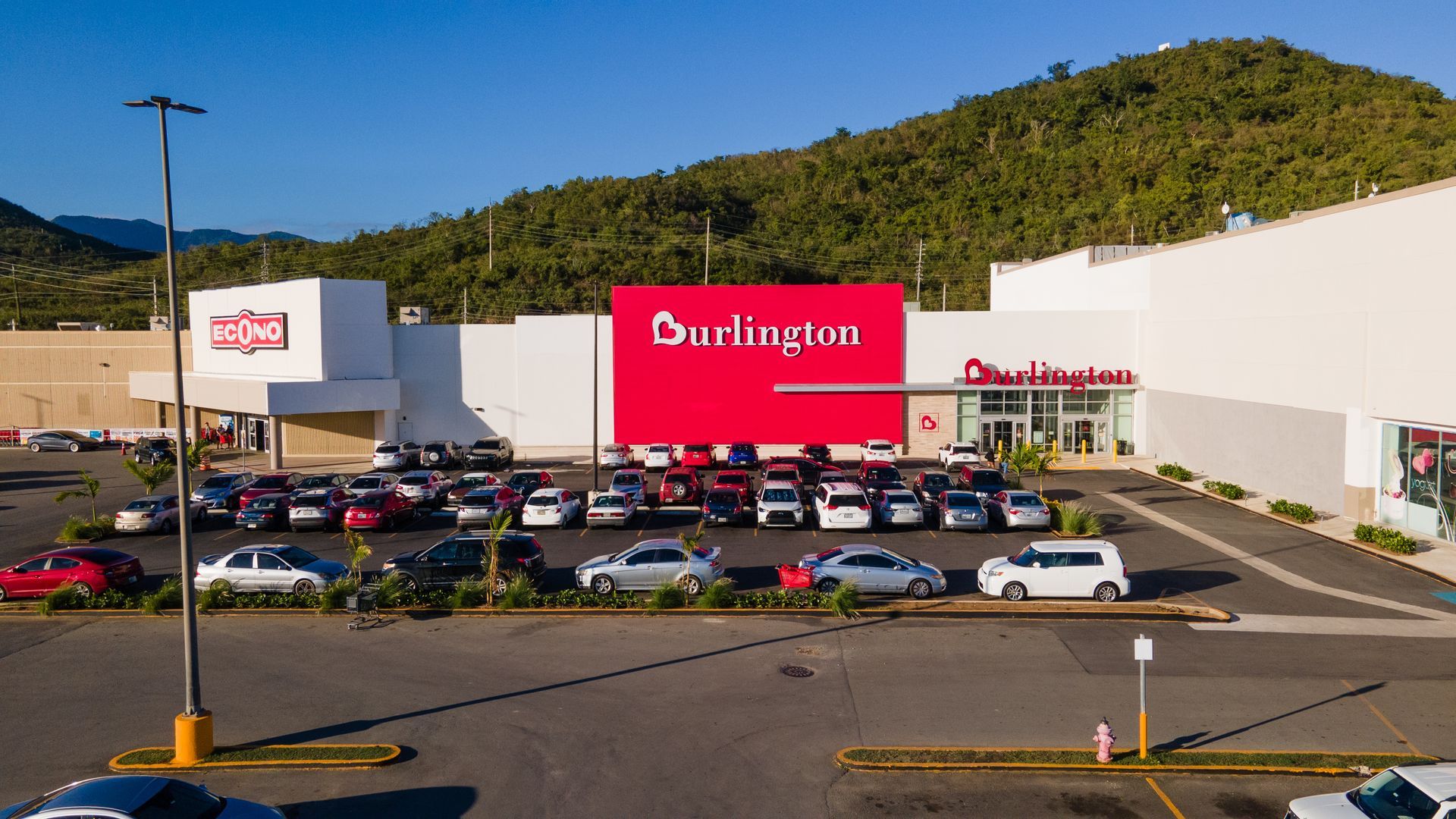 Burlington store exterior with parked cars, set against a green mountain backdrop. Red Burlington sign.
