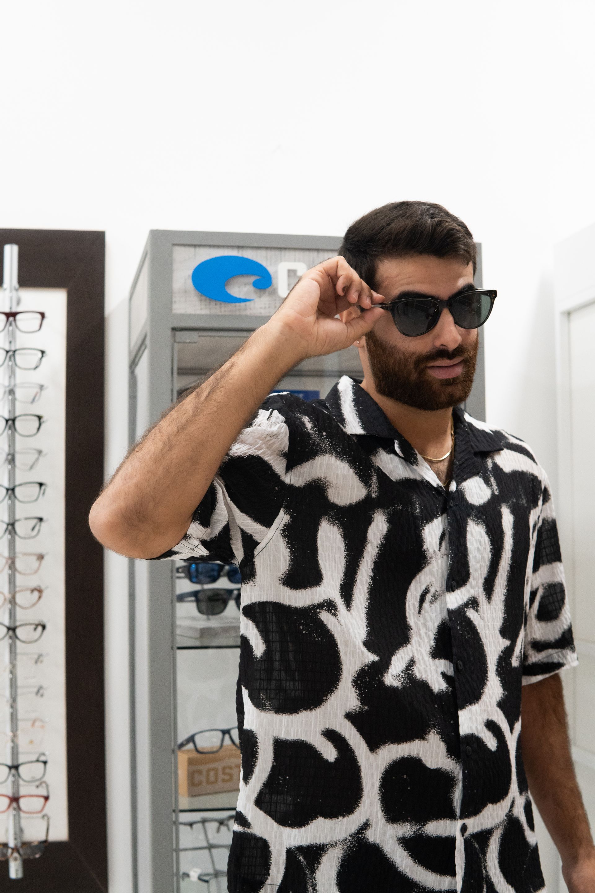 A person in a black dress and white bag descends a mall escalator, smiling towards the camera.