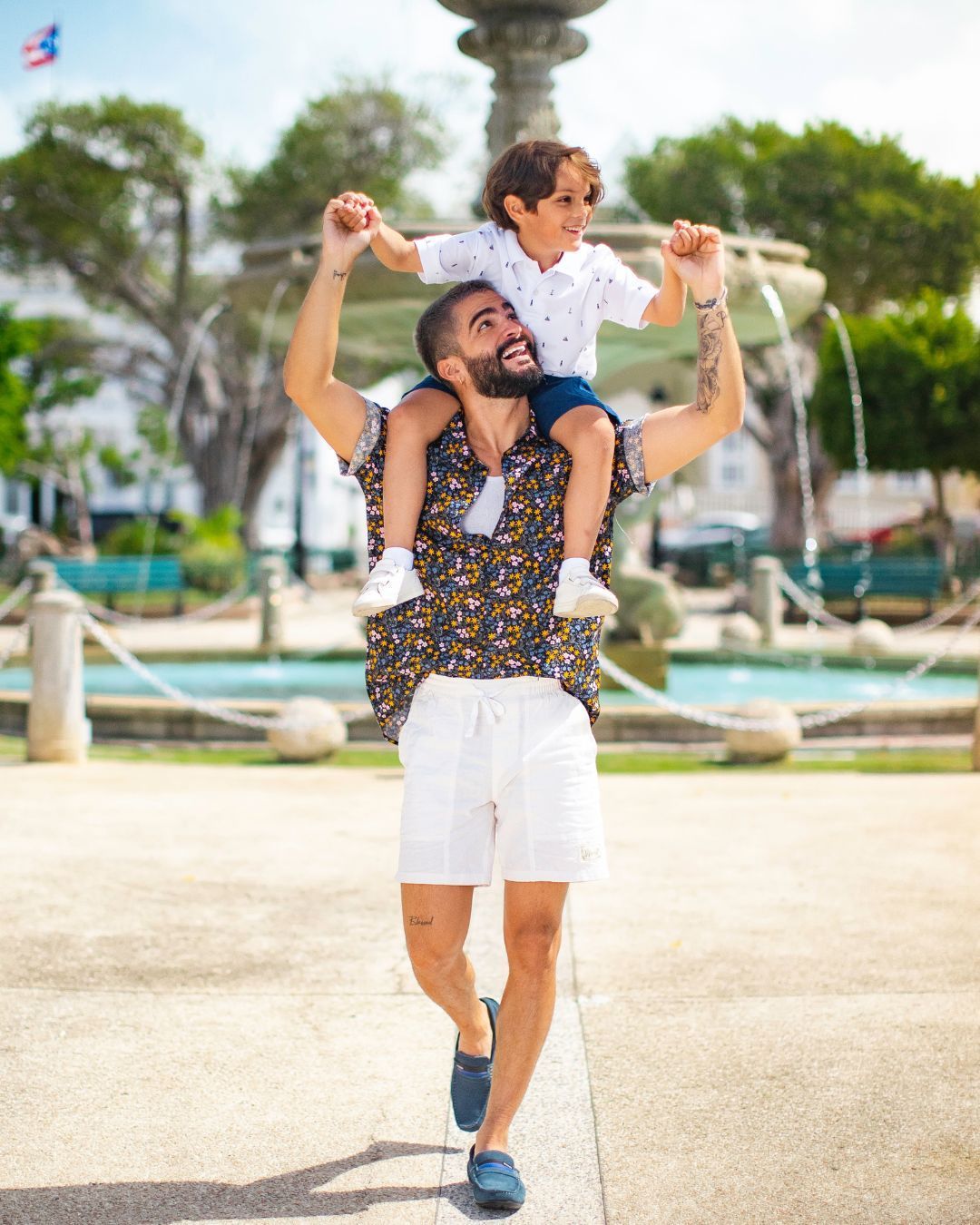 A man is carrying a little boy on his shoulders in front of a fountain.