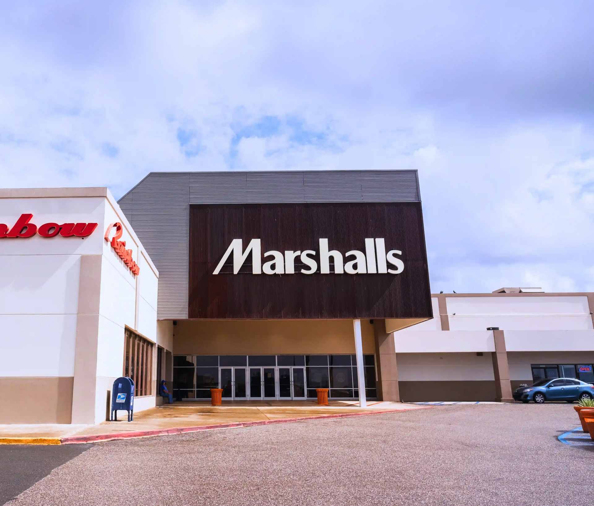 Exterior of a Marshalls store with a Rainbow store on the left, under a cloudy sky.
