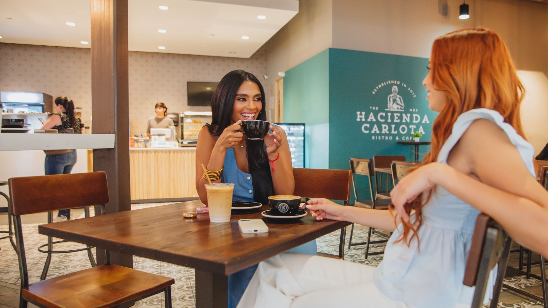 Two women at a cafe table, one drinking coffee.