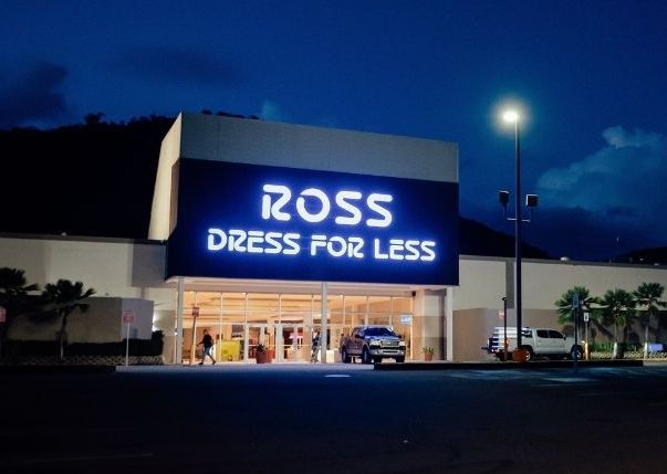 Ross Dress for Less store front lit at night with white sign and entrance, parked cars in lot.