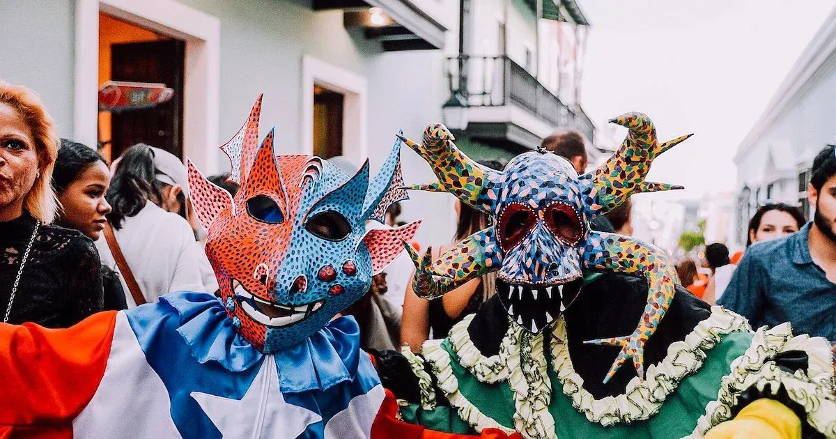 Two costumed figures in masks, parade: red, blue, and white; green and yellow, street setting.