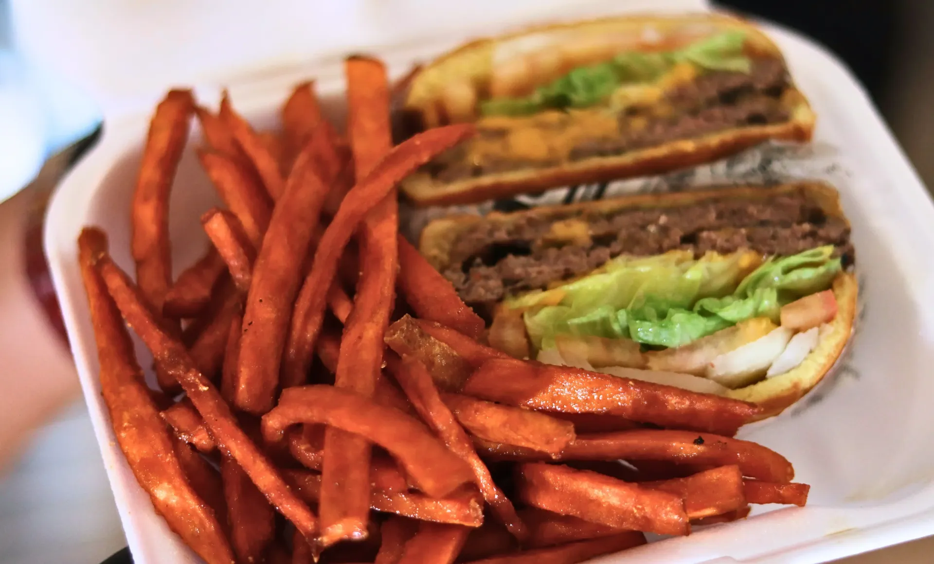 Burger with sweet potato fries in a takeout container.
