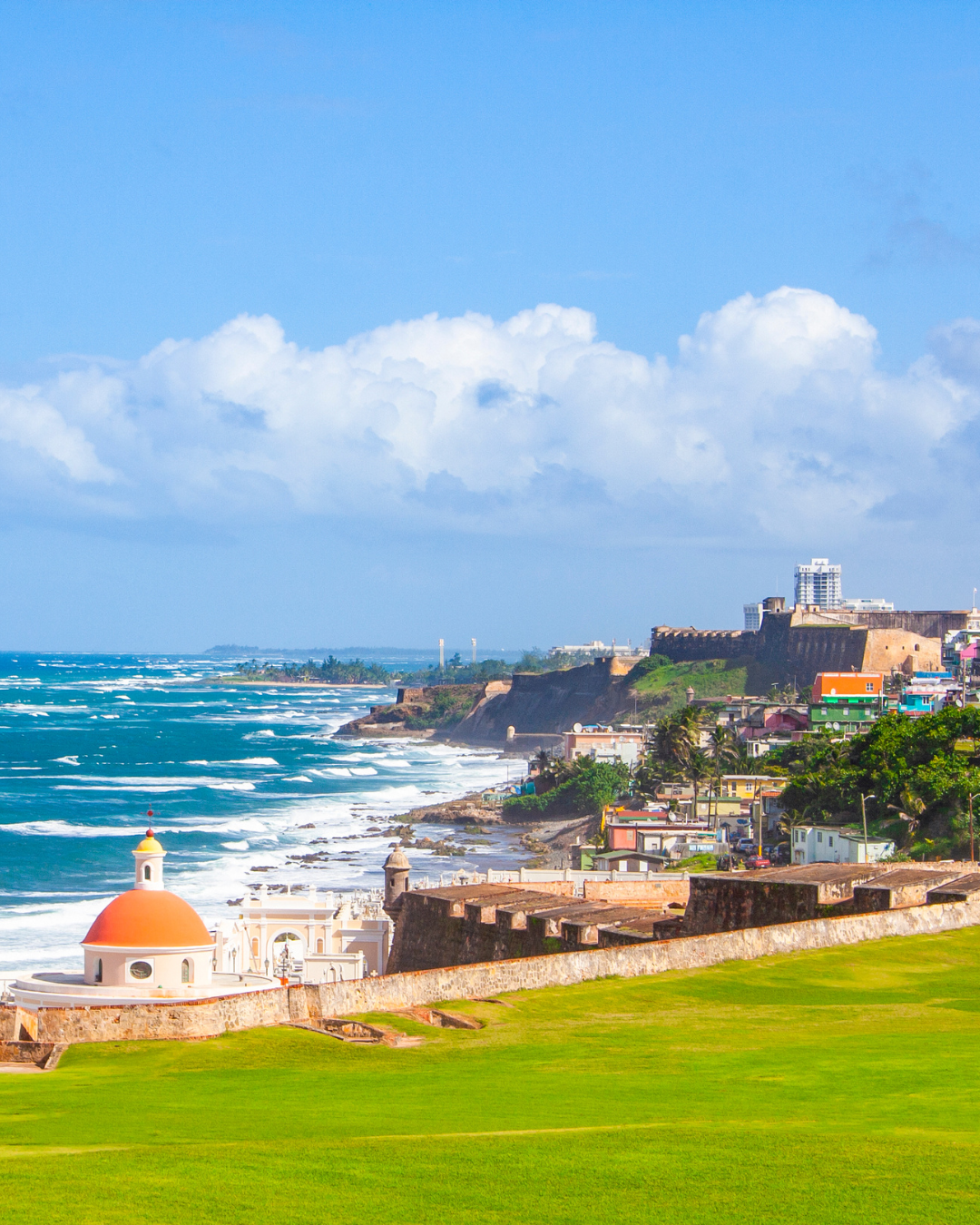 San Juan Puerto Rico with historic stone fort and church on a sunny day with blue sky and ocean waves.