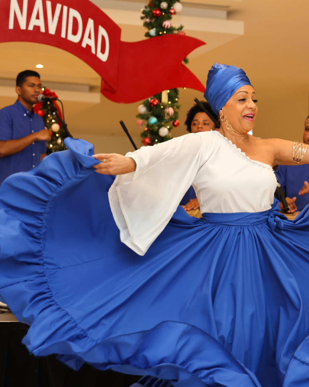 A group of people performing a dance, with a Feliz Navidad banner in front of them.