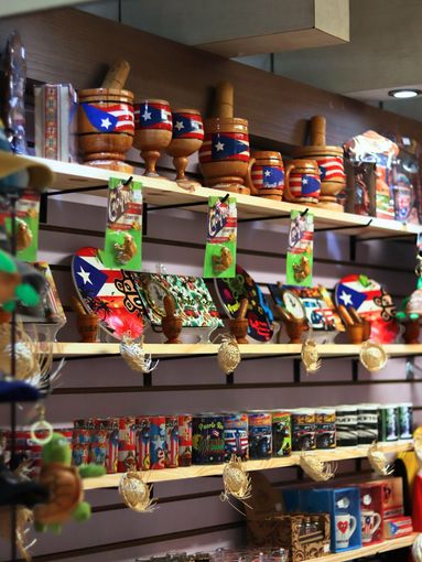 Shelves displaying Puerto Rican souvenirs: mugs, plates, wooden mortar and pestle sets decorated with the Puerto Rican flag.
