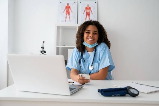 A female nurse sitting in a clinic with her laptop in front