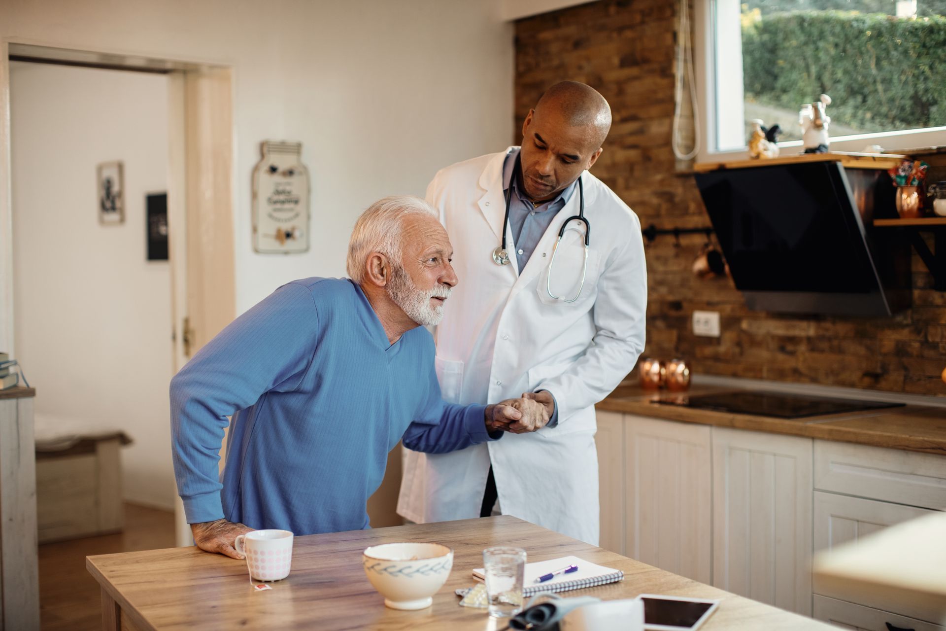 Doctor helping an elderly man stand in a kitchen, illustrating aged care jobs in regional Australia