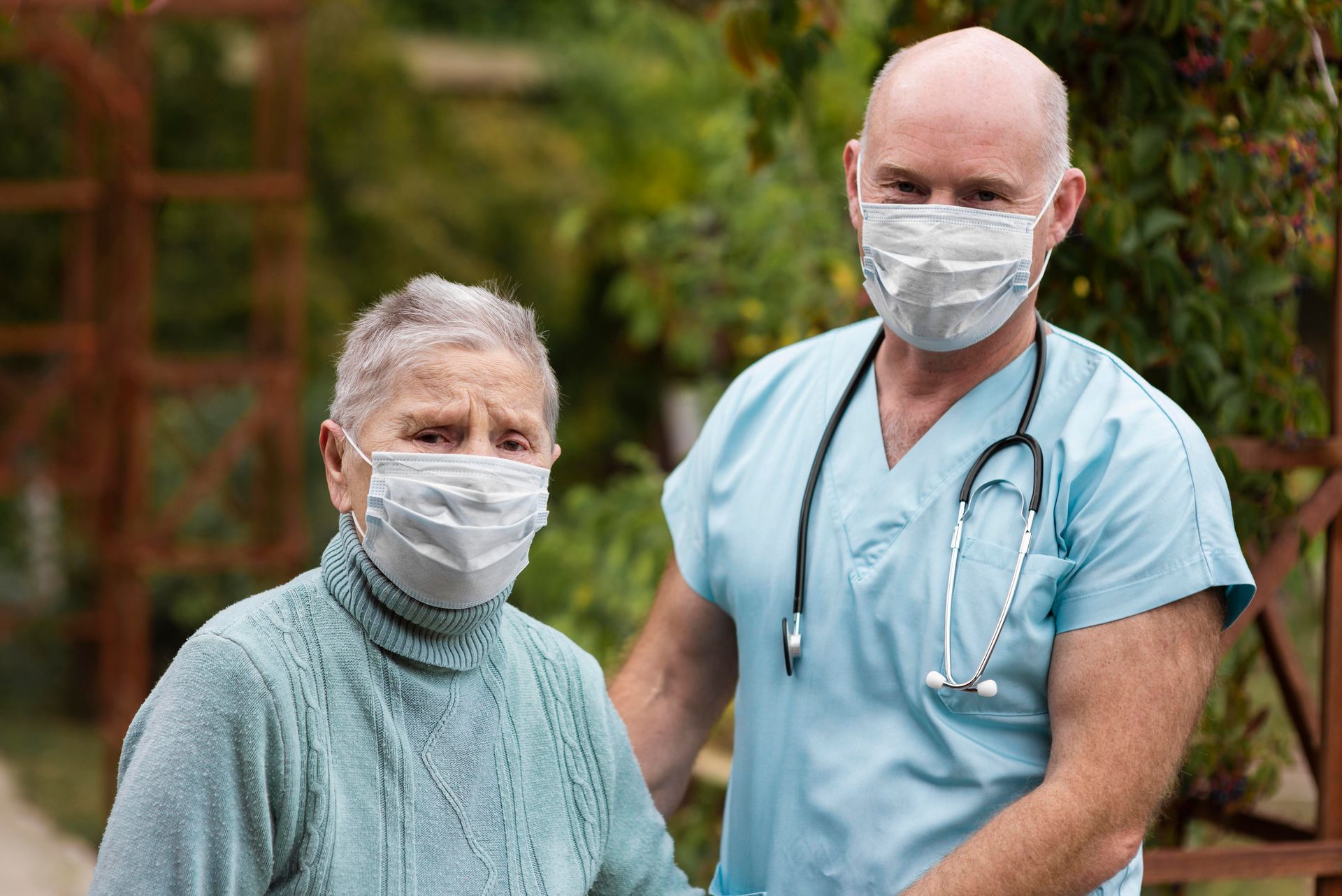 A healthcare worker with a stethoscope standing beside an elderly man