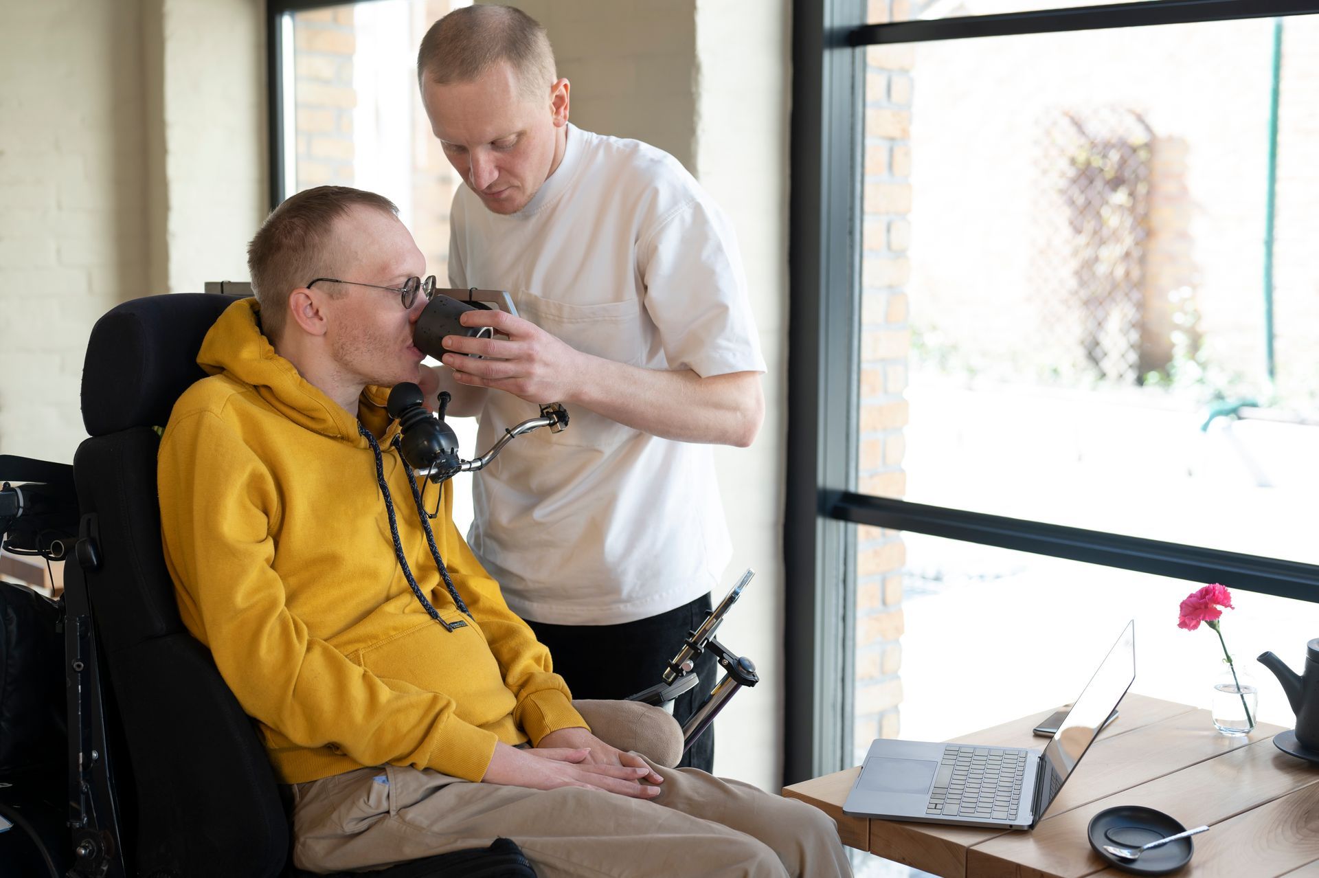 Disability support worker helping client in wheelchair drink water during daily care routine under NDIS