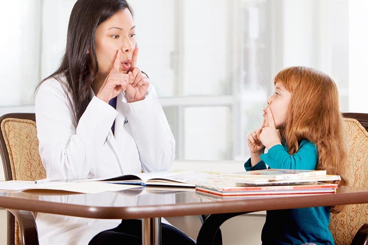 A healthcare professional teaching a kid how to communicate in a home setting