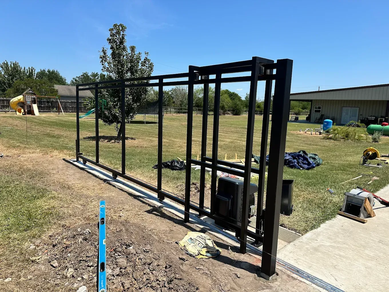 A black sliding gate is being built in a yard.