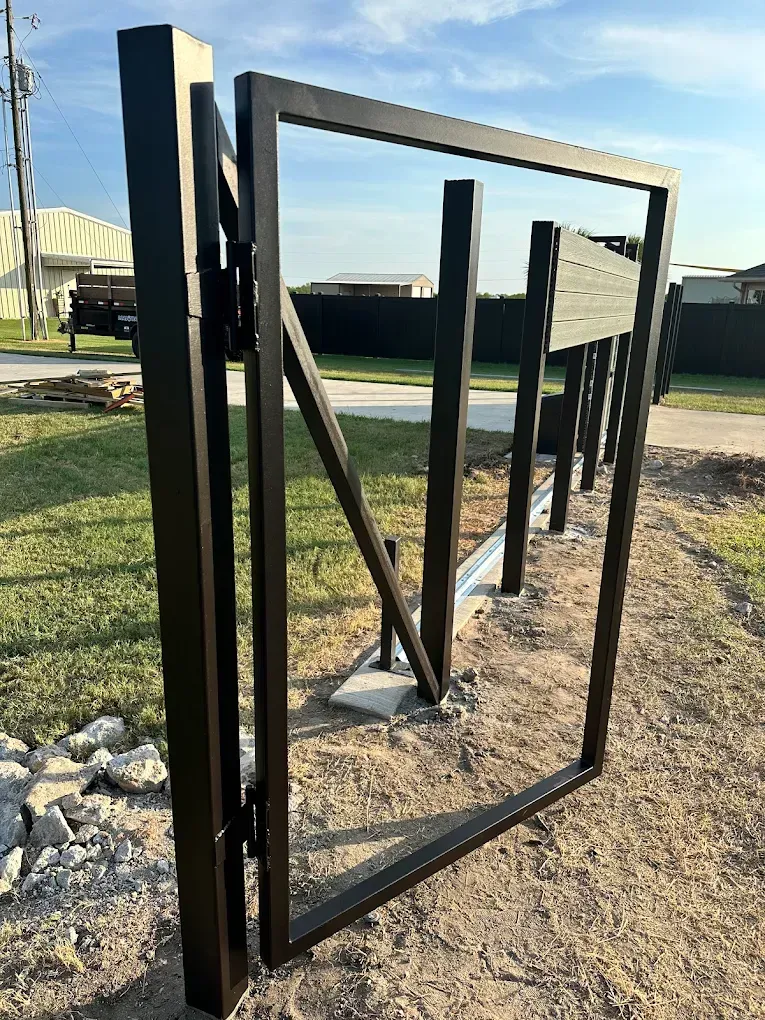 A black metal gate is sitting on top of a dirt field.