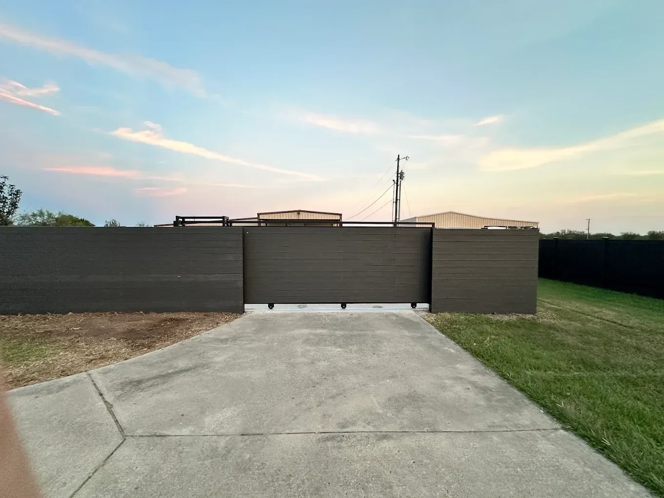A driveway leading to a house with a fence and a sliding gate.