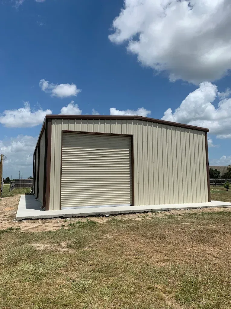 A metal building with a garage door is sitting in the middle of a grassy field.