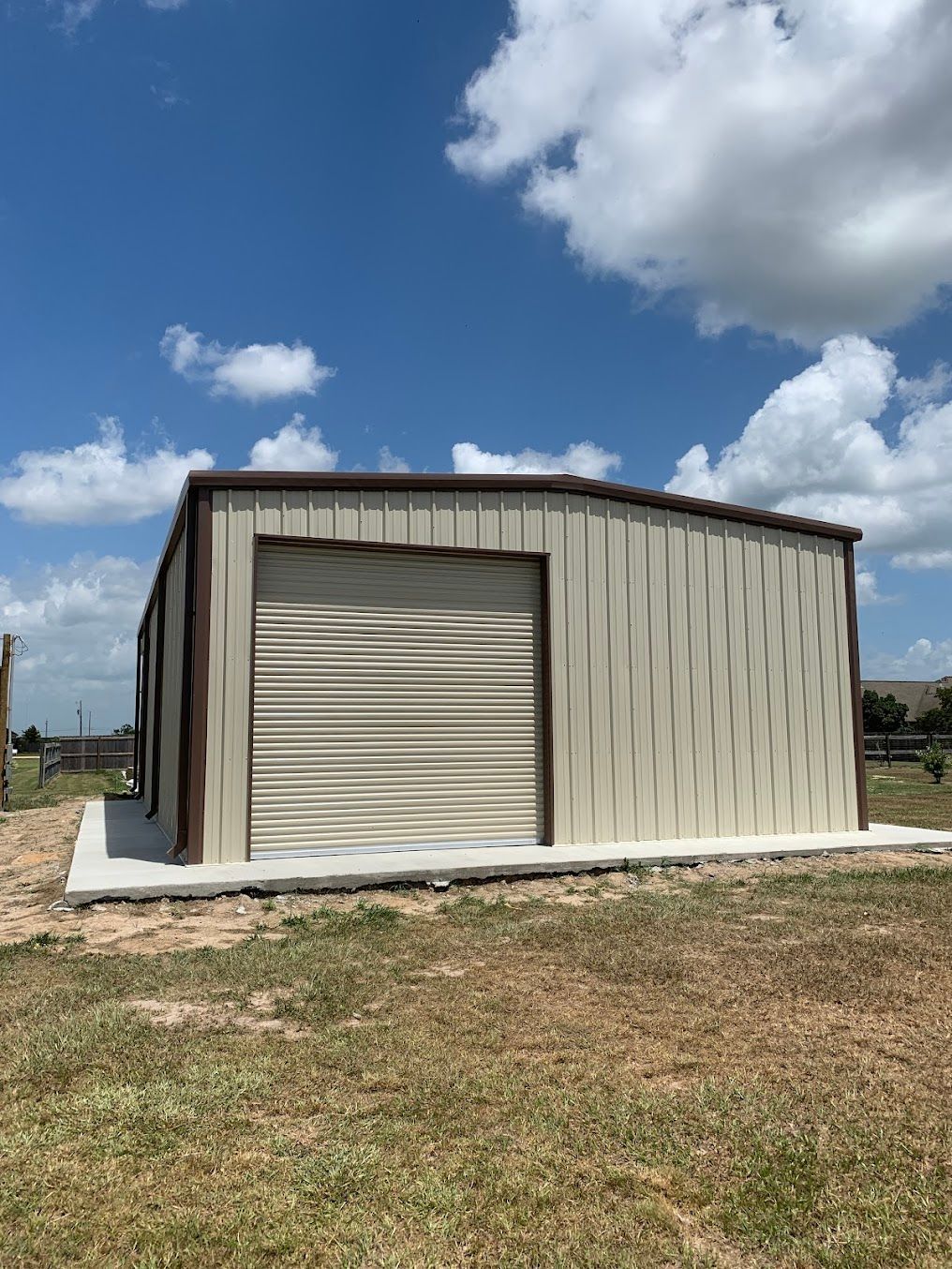 A metal garage with a roll up door is sitting in the middle of a grassy field.