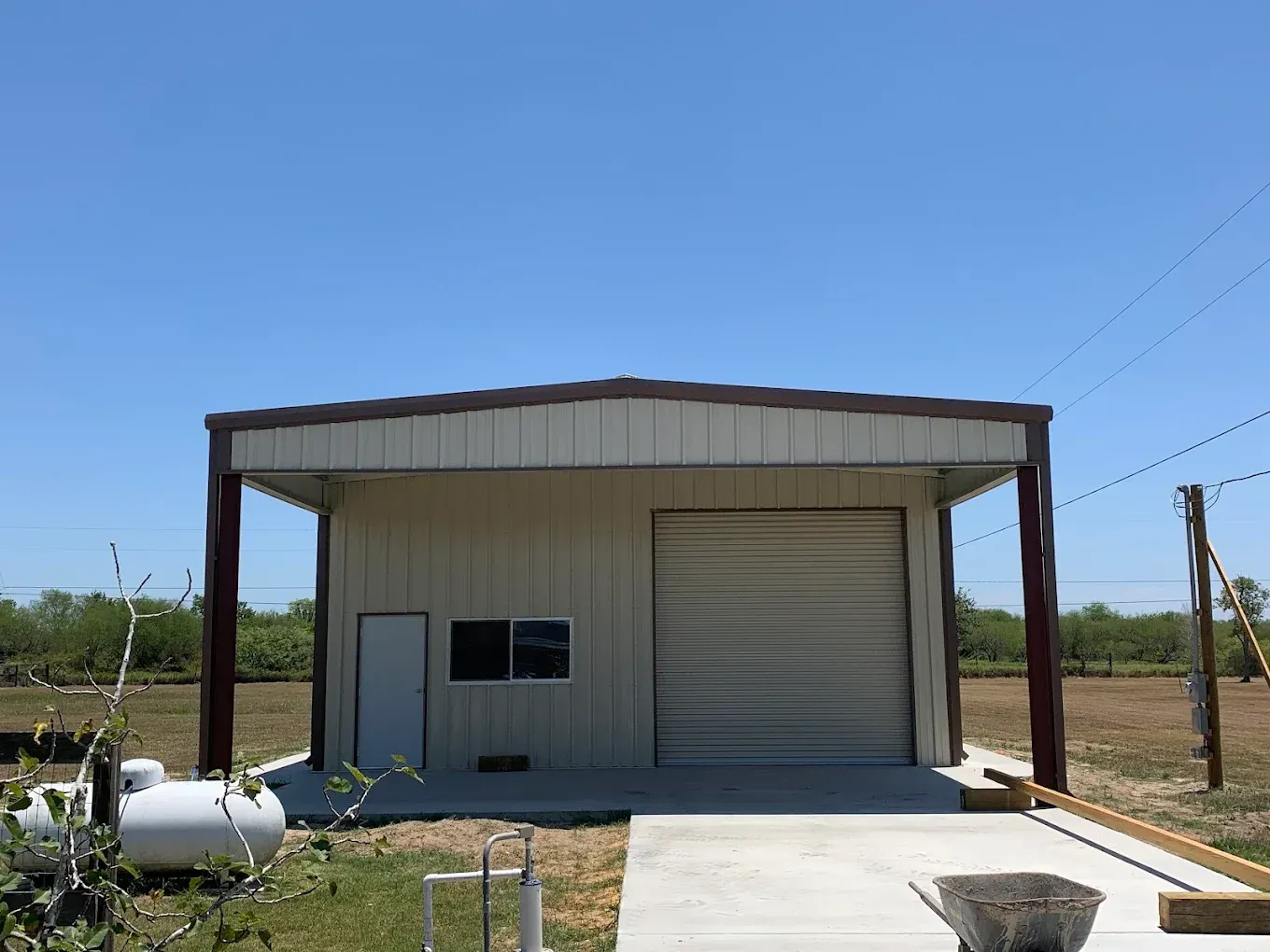 A metal building with a garage door is sitting in the middle of a field.