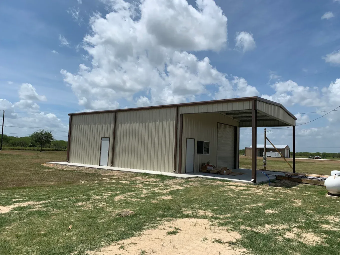 A metal building with a canopy is sitting in the middle of a grassy field.